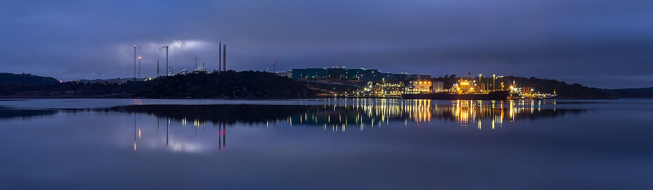 Oil refinery facility at dusk with illuminated processing units and flare stacks.